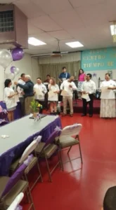 A group of people gathered around tables, decorated with purple balloons, engaged in conversation and celebration.