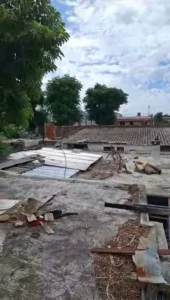 A roof covered with debris and fallen branches, indicating recent storm damage and surrounding trees.