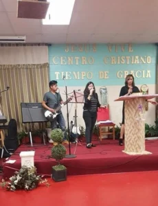 Three people performing on a stage at a church event with musical instruments and a microphone