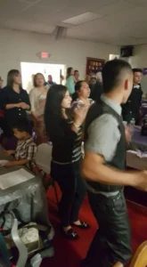 A group of people gathered around a table, watching a man and woman dance joyfully in the center of the scene.