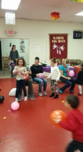 A group of children joyfully playing with colorful balloons in a bright, spacious room.