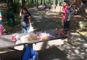 A group of individuals gathered around a picnic table in a tranquil forest, sharing food and conversation